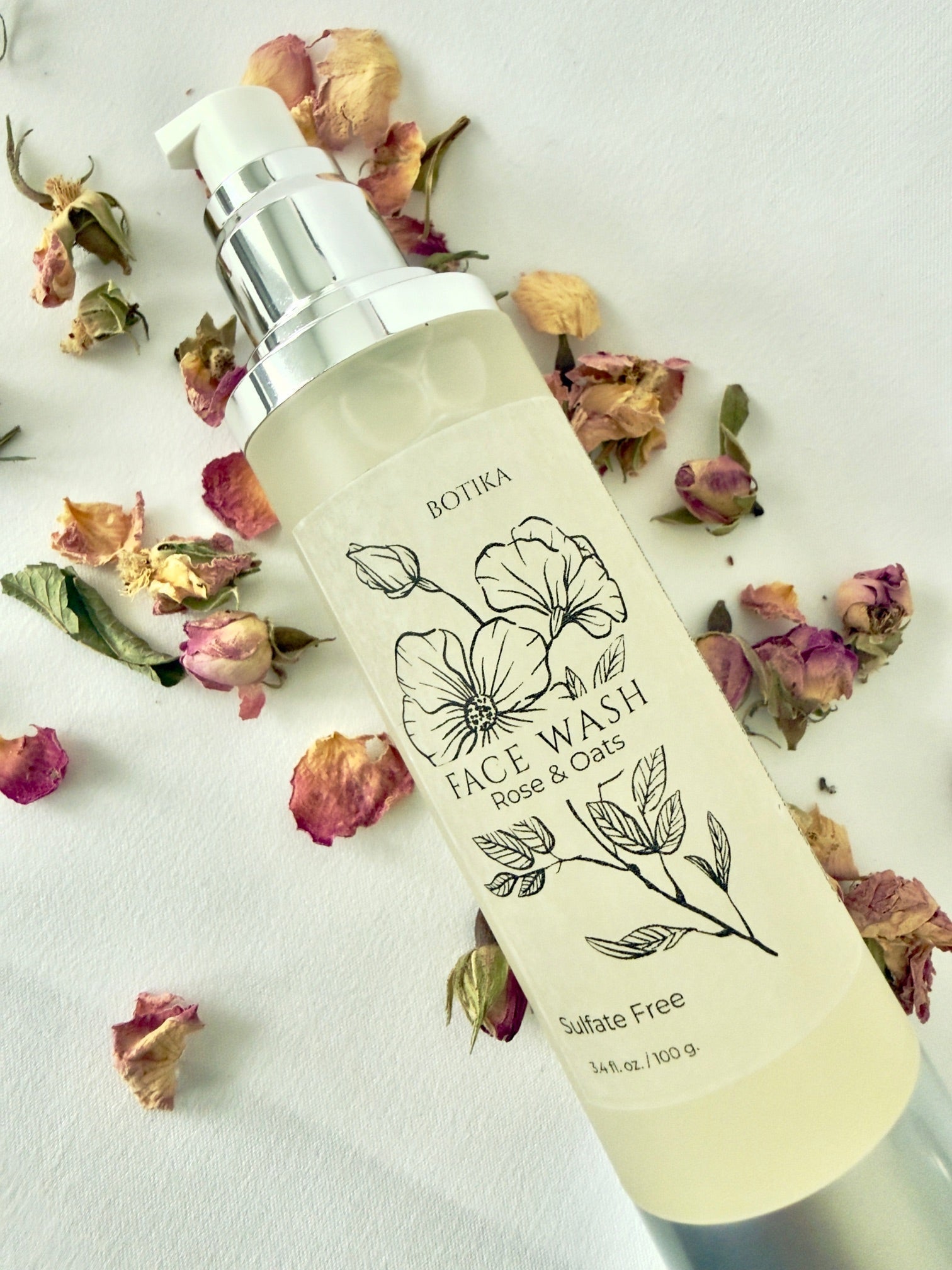 Botika Skincare Rose & Oat Gentle Face Wash for Sensitive Skin  bottle resting on surface surrounded by dried roses and oats