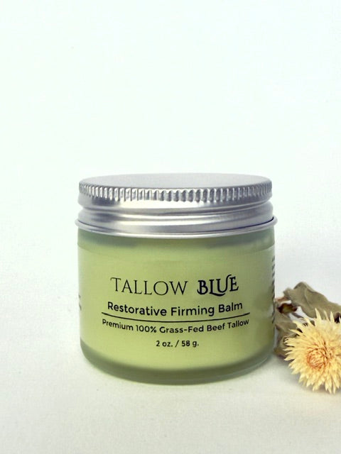 Tallow Blue Restorative Firming Balm jar on a white background with a dried flower.
